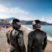 Firefly backs of two men in black motorcycle helmets on a beach near Naples Italy terrified beachg