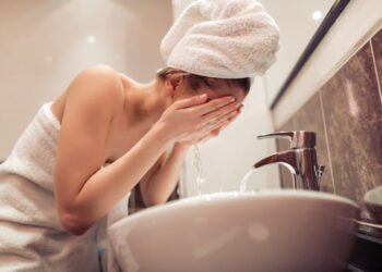 Young woman washing face with water in bathroom.