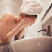 Young woman washing face with water in bathroom.